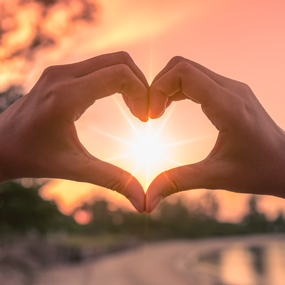 Hands in heart shape over sunset image